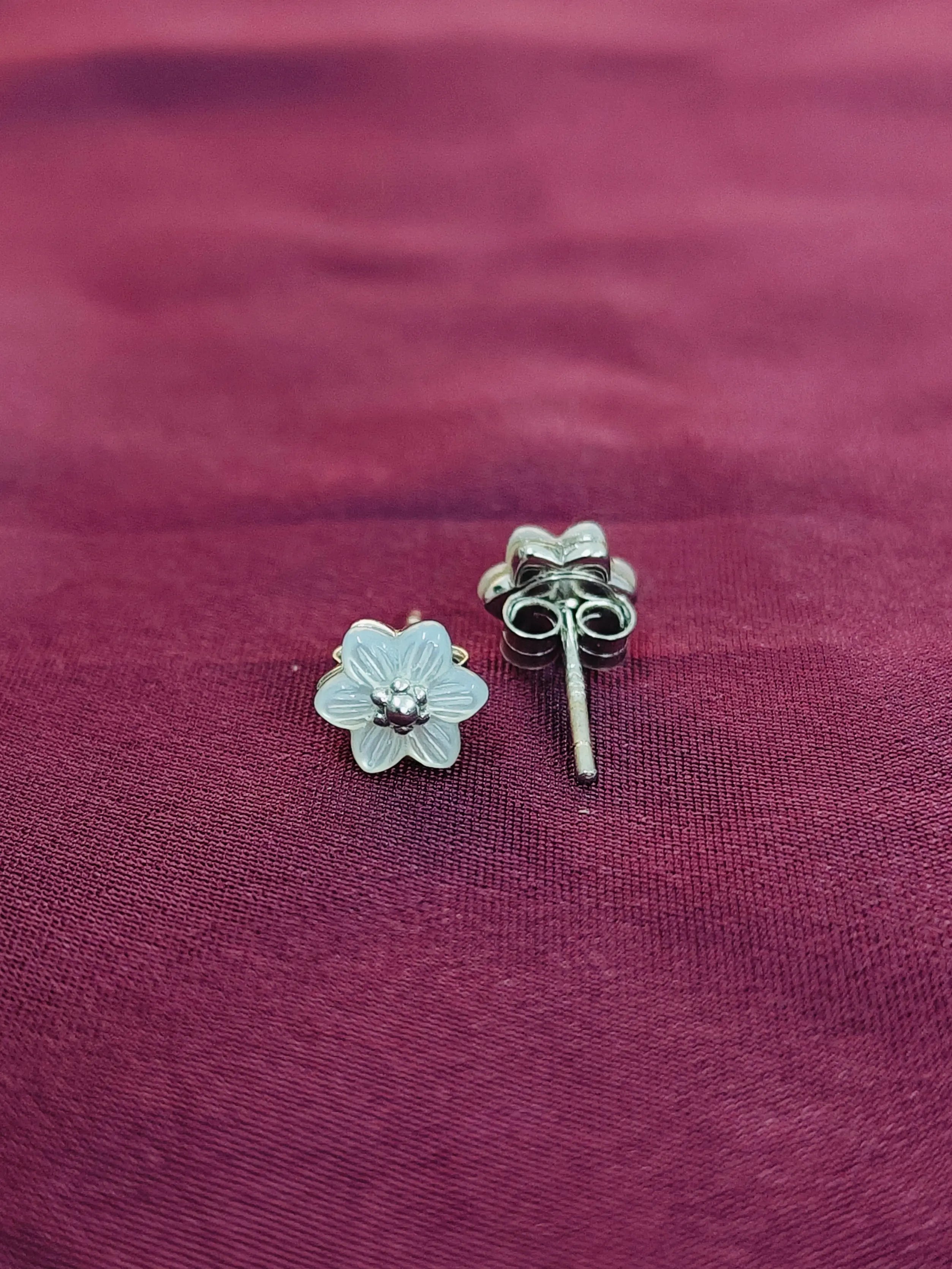 Silver flower-shaped earring and straight post earring on a purple fabric background